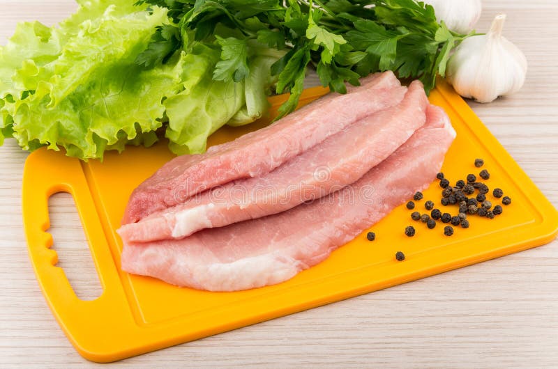 Pieces of Raw Pork on Board, Greens, Garlic and Pepper Stock Photo