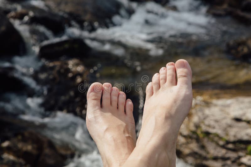 Piedi del ` s della donna davanti al fiume selvaggio della montagna immagini stock libere da diritti Piedi del ` s della donna davanti al fiume selvaggio della montagna immagini stock libere da diritti