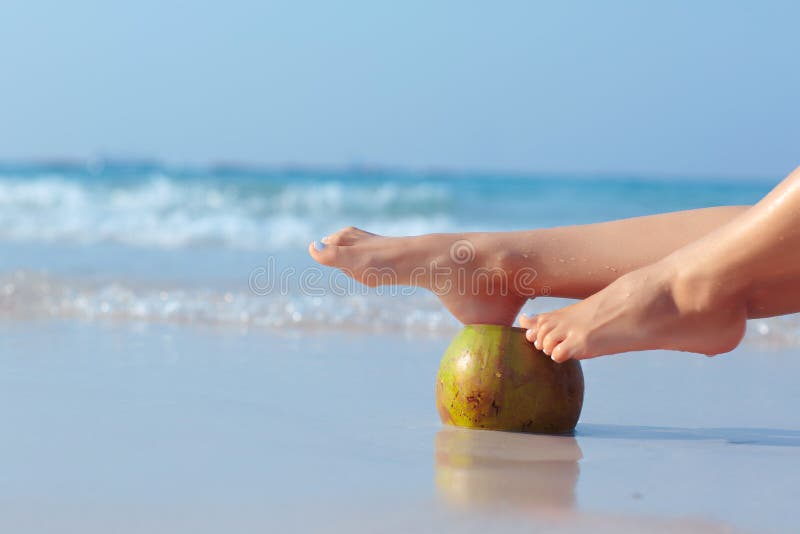 Piedi femminili propped sulla noce di cocco sul fondo del mare immagini stock Piedi femminili propped sulla noce di cocco sul fondo del mare immagini stock