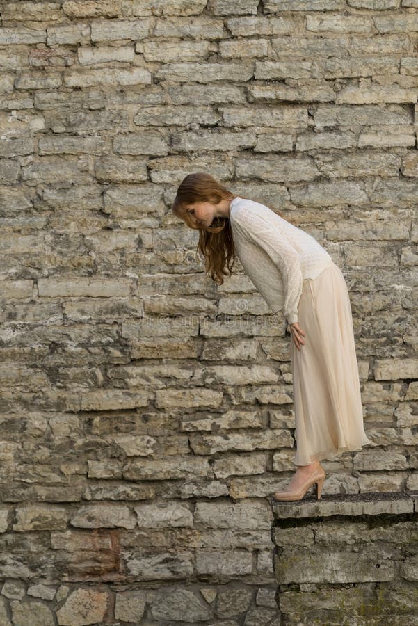 Piedra femenina blanca caucásica del modelo y del ladrillo Muchacha hermosa, pelo rojo largo, falda beige y rebeca Mujer que se c imagen de archivo libre de regalías Piedra femenina blanca caucásica del modelo y del ladrillo Muchacha hermosa, pelo rojo largo, falda beige y rebeca Mujer que se c imagen de archivo libre de regalías