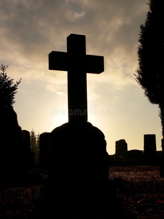 The sun setting behind a crossshaped tombstone on a graveyard at Halloween. The sun setting behind a crossshaped tombstone on a graveyard at Halloween