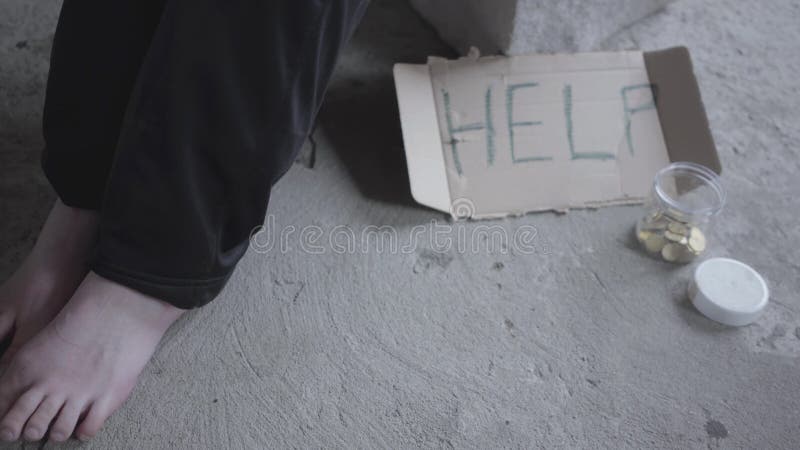 Pieds de la pauvre fille aux pieds nus s'asseyant dans un vide poussiéreux dans le bâtiment abandonné Un signe qui indique l'aide