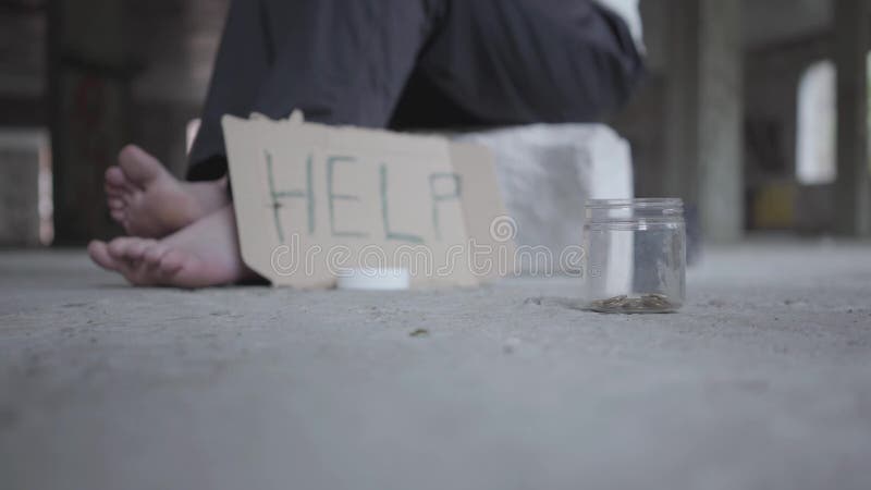 Pieds de pauvre fille aux pieds nus sur le plancher en béton Un signe brouillé qui indique l'aide et le pot avec des pièces de mo