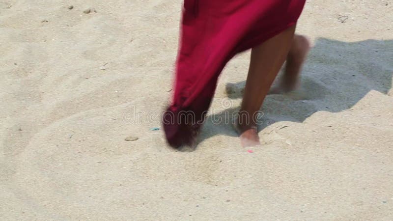 Pieds féminins sur le sable dans une robe rouge en développement. un clips vidéos