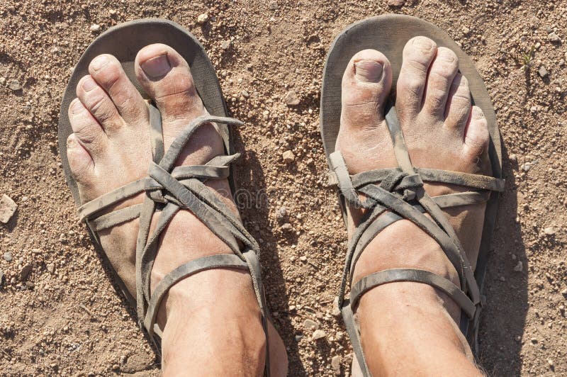 Closeup POV of dusty male feet in traditional rustic leather strap sandals standing on dry barren ground. Closeup POV of dusty male feet in traditional rustic leather strap sandals standing on dry barren ground