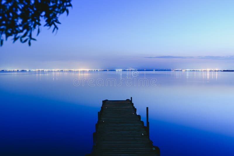 Pier en un lago al atardecer con agua tranquila y reflejos de luces relajantes