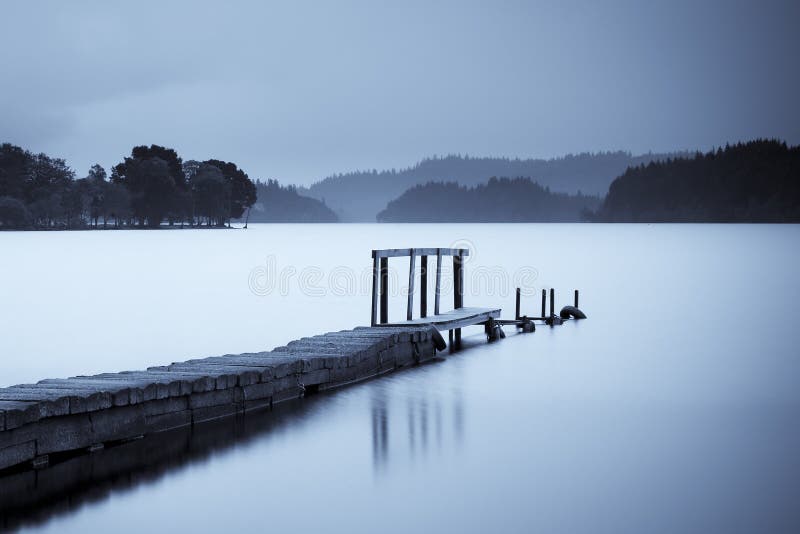 Scenic view of pier on Loch Ard with silhouetted shoreline at dawn, Scotland.