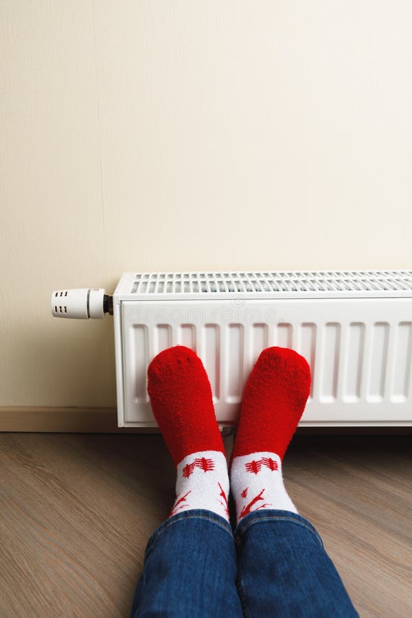 Legs with red Christmas deer socks in front of heating radiator, close-up view. Legs with red Christmas deer socks in front of heating radiator, close-up view