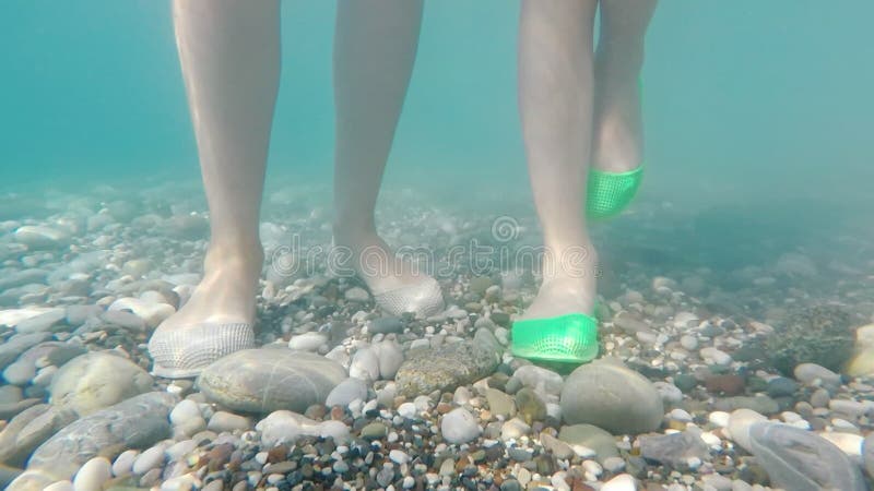 Piernas con zapatos de protección en el fondo del mar de guijarros. baño seguro en el mar
