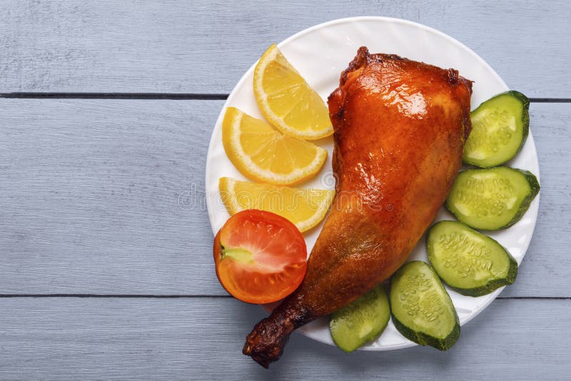 Piernas de pollo curruscantes, asadas en una parrilla con el limón, el pepino y los tomates cortados en la placa blanca en una ta imágenes de archivo libres de regalías Piernas de pollo curruscantes, asadas en una parrilla con el limón, el pepino y los tomates cortados en la placa blanca en una ta imágenes de archivo libres de regalías