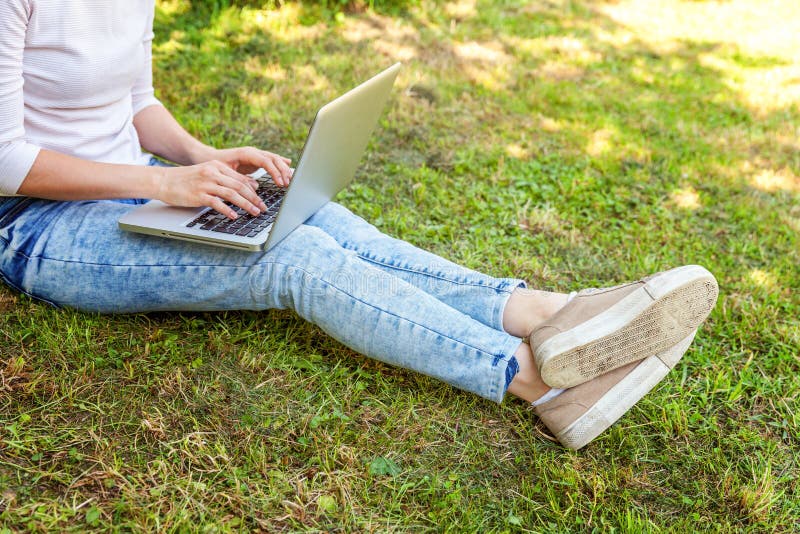Piernas en c?sped de la hierba verde en parque de la ciudad, manos de la mujer que trabajan en el ordenador de la PC del ordenado fotografía de archivo Piernas en c?sped de la hierba verde en parque de la ciudad, manos de la mujer que trabajan en el ordenador de la PC del ordenado fotografía de archivo
