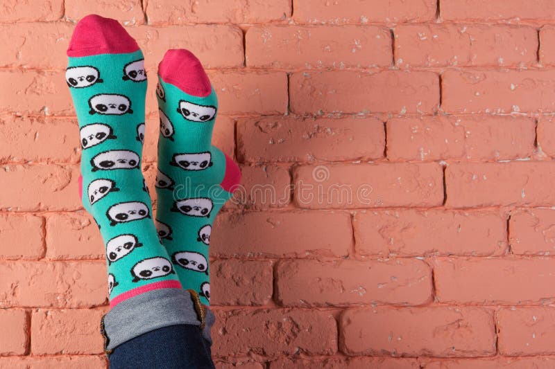 Legs in turquoise socks with a picture of panda faces, leaning on a brick wall, grow up, concept, copy space. Legs in turquoise socks with a picture of panda faces, leaning on a brick wall, grow up, concept, copy space