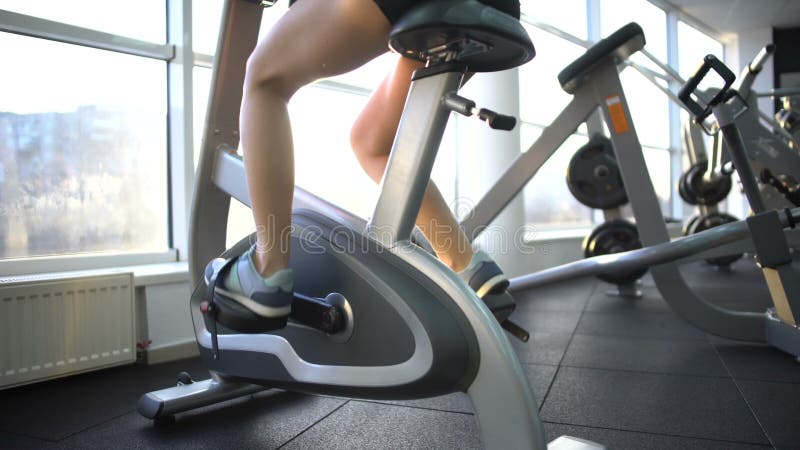 Piernas femeninas que entrenan en la bici inmóvil, calorías ardientes, ejercicio cardiio