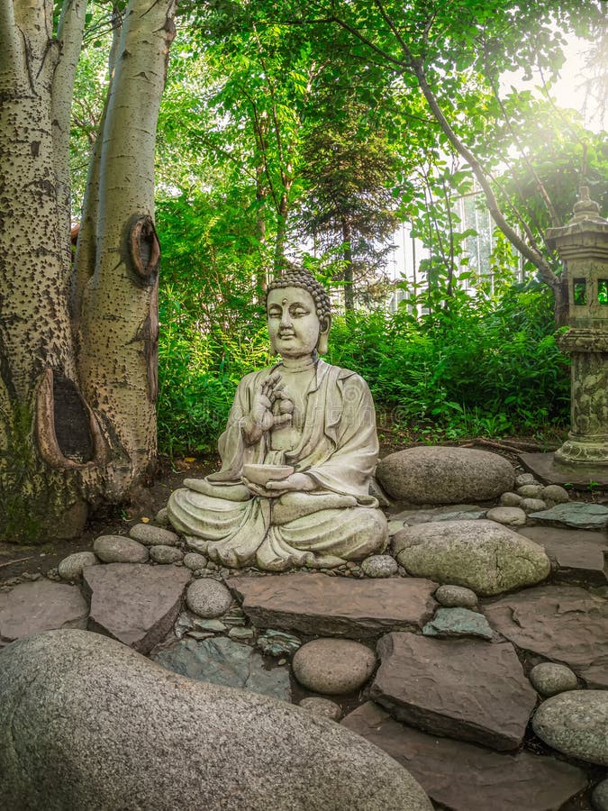 Pierre gautama bouddha statue décorative dans un jardin sous feuilles vertes. concept de décoration de jardin extérieur. vue verti photo libre de droits