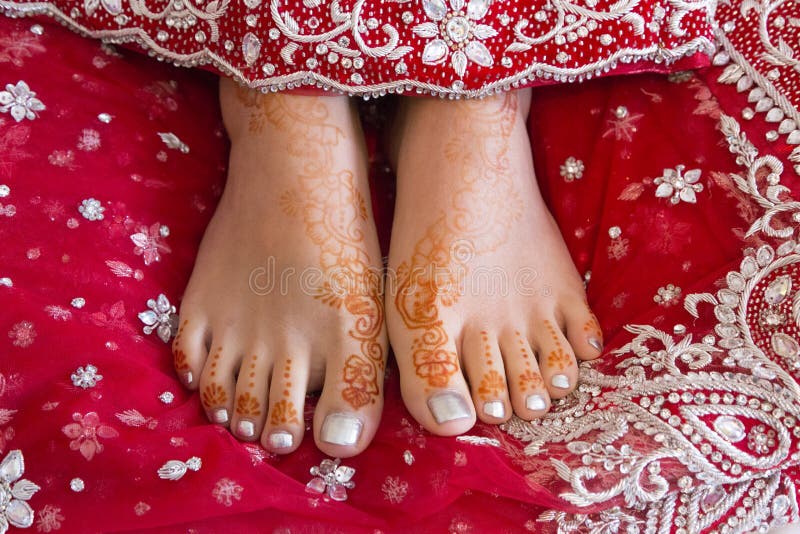 Indian brides henna tattooed feet rest on red wedding dress. Indian brides henna tattooed feet rest on red wedding dress