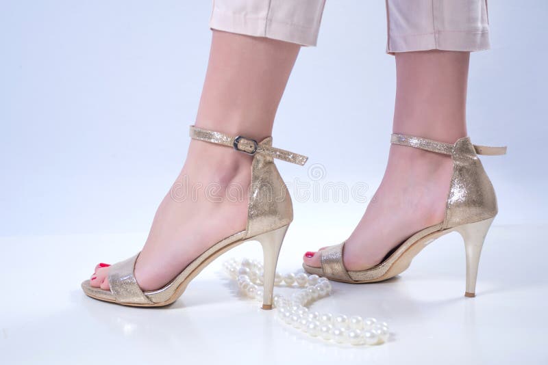 Pies desnudos de la mujer en tacones altos y collar de oro de las perlas en el fondo blanco imagen de archivo Pies desnudos de la mujer en tacones altos y collar de oro de las perlas en el fondo blanco imagen de archivo