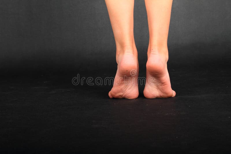 Barefoot teenage girl - schoolkid with healthy bare feet standing on tiptoes on black background. Body part concept. Barefoot teenage girl - schoolkid with healthy bare feet standing on tiptoes on black background. Body part concept.