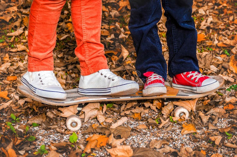 Pies en zapatillas de deporte en un otoño de los niños del monopatín dos foto de archivo Pies en zapatillas de deporte en un otoño de los niños del monopatín dos foto de archivo