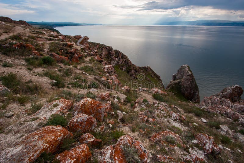 Pietre con muschio rosso sulle rocce del lago Baikal sull'isola di Olkhon Fra l'erba verde delle pietre Montagne dietro il lago fotografia stock Pietre con muschio rosso sulle rocce del lago Baikal sull'isola di Olkhon Fra l'erba verde delle pietre Montagne dietro il lago fotografia stock