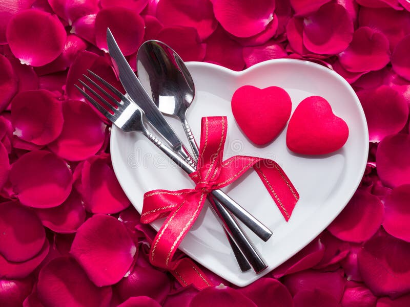 Pietre di rosa rosa rosa sul piatto a forma di cuore forchetta, coltello e cucchiaio legati con nastro rosso fotografie stock libere da diritti Pietre di rosa rosa rosa sul piatto a forma di cuore forchetta, coltello e cucchiaio legati con nastro rosso fotografie stock libere da diritti