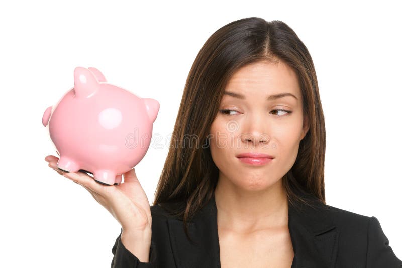 Piggy bank savings with unhappy funny woman looking displeased at pink piggy bank isolated on white background. Business woman or banker wearing suit jacket. Mixed race Asian Caucasian female model.