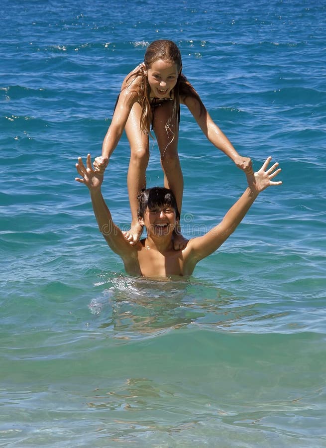Portrait of a brother and sister in summer party at sea. Sister standing on the shoulders (piggy back) of her brother in crystal clear blue green Adriatic sea. (Croatia-Dalmatia). Vertical color photo. Portrait of a brother and sister in summer party at sea. Sister standing on the shoulders (piggy back) of her brother in crystal clear blue green Adriatic sea. (Croatia-Dalmatia). Vertical color photo.