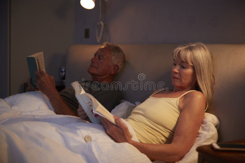 Pijamas vestindo dos pares superiores que encontram-se na leitura da cama fotos de stock Pijamas vestindo dos pares superiores que encontram-se na leitura da cama fotos de stock