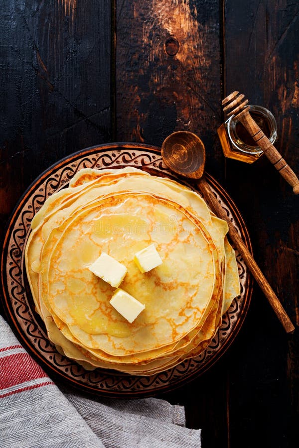 Pila de crepes finas hechas en casa con los pedazos de mantequilla, de leche y de miel en la placa de cerámica rústica vieja imágenes de archivo libres de regalías Pila de crepes finas hechas en casa con los pedazos de mantequilla, de leche y de miel en la placa de cerámica rústica vieja imágenes de archivo libres de regalías