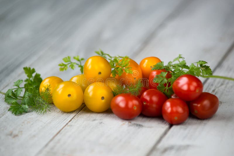 Pila de naranja mezclada, de amarillo y de rojo de los tomates de cereza con las hierbas frescas en un fondo de madera fotografía de archivo Pila de naranja mezclada, de amarillo y de rojo de los tomates de cereza con las hierbas frescas en un fondo de madera fotografía de archivo