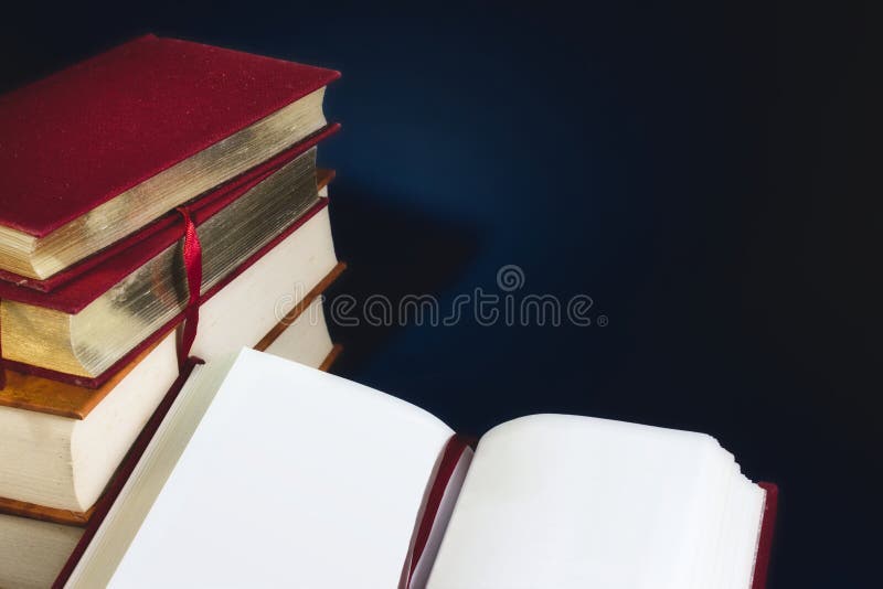 Pila di vecchi libri e di libro aperto con le pagine vuote in bianco contro un fondo blu scuro immagini stock libere da diritti Pila di vecchi libri e di libro aperto con le pagine vuote in bianco contro un fondo blu scuro immagini stock libere da diritti