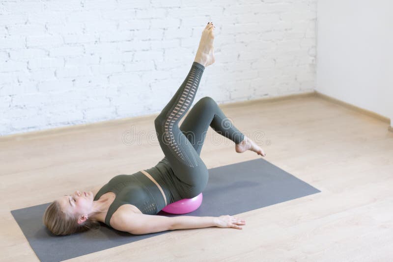 Pilates, leg arch exercise. Young caucasian fit woman doing work out with small pink fitness ball on the floor in loft