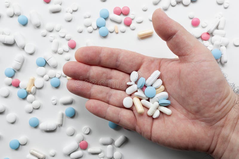 Pile of blue, white, pink and yellow colored pills and capsules with male hand