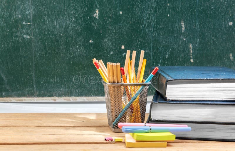 Pile of books with notes paper and pen with pencils in basket container on wooden table with chalkboard background