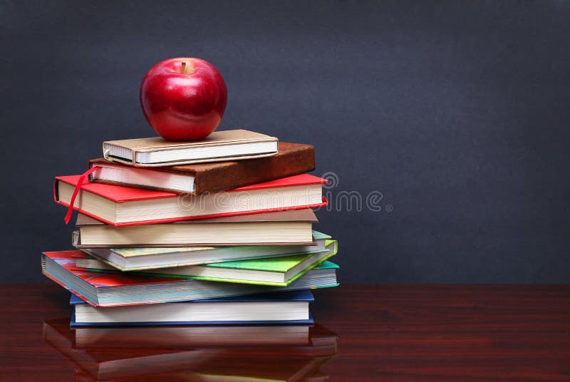Pile of books and red apple on the desk over the blackboard royalty free stock photo