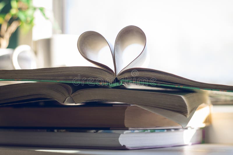 Stack of books with open one at the top. Heart of pages on background of open window. Love reading concept. Stack of books with open one at the top. Heart of pages on background of open window. Love reading concept