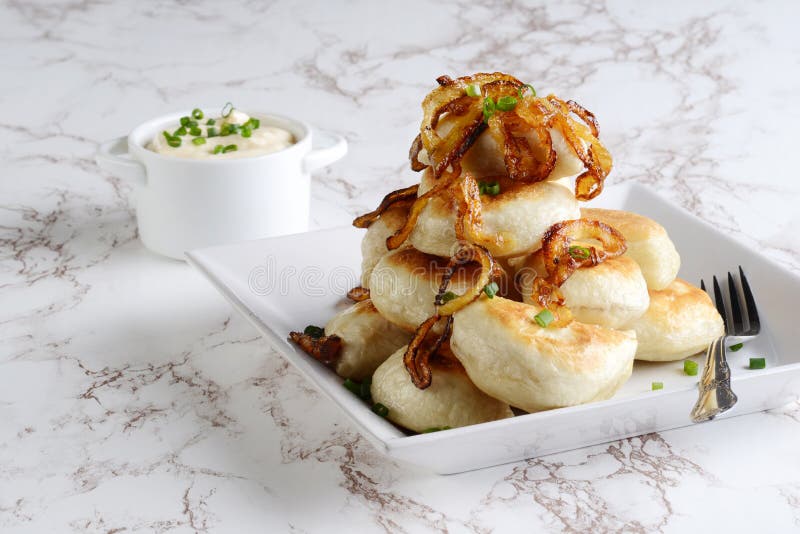 Pile of pierogies with sour cream caramelized onions and a fork