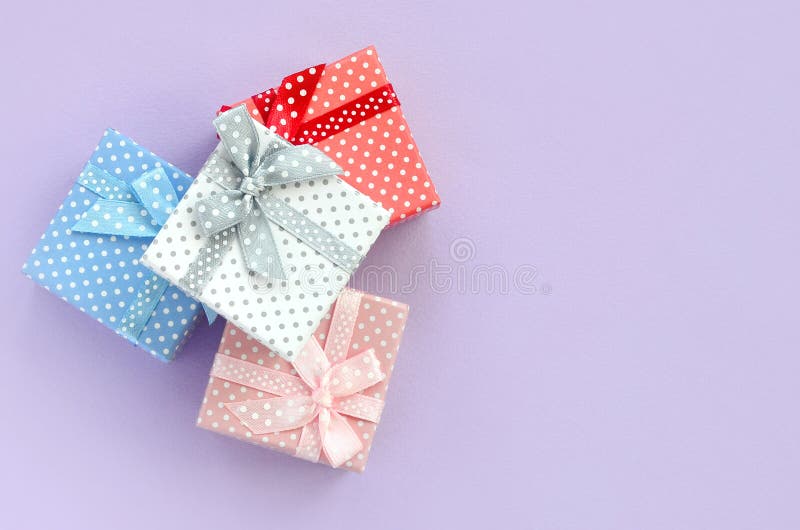 Pile of a small colored gift boxes with ribbons lies on a violet background. Minimalism flat lay top view