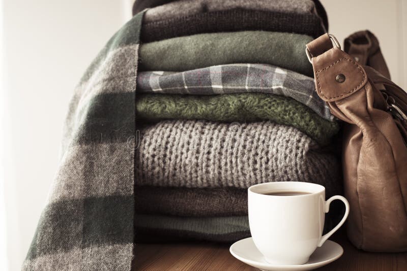 Pile of sweaters, leather bag and a hot coffee cup