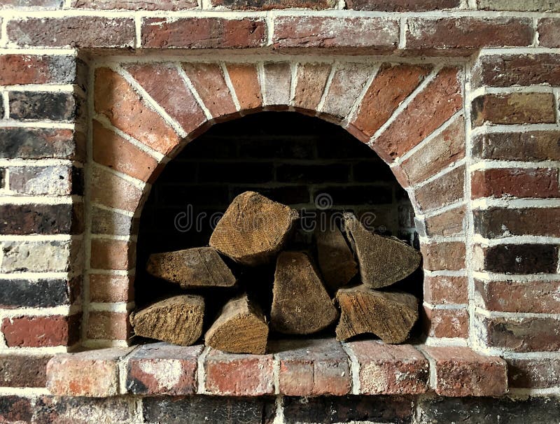 A pile of logs are stacked inside an opening in a brick fireplace wall f