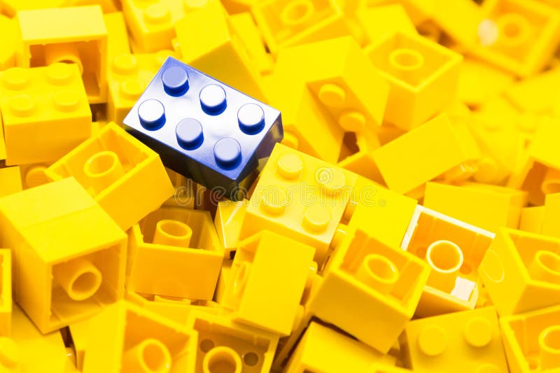 Pile of yellow color building blocks with selective focus and highlight on one particular blue block using available light