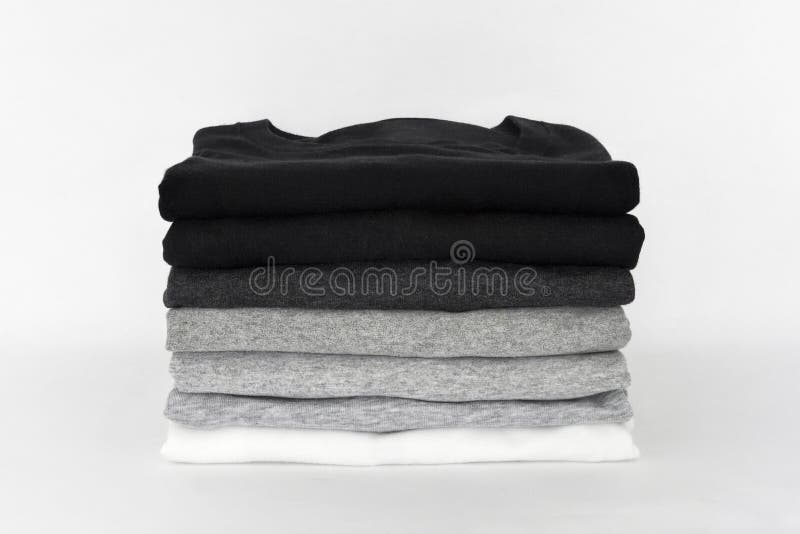 Pilha de t-shirt monocromático dobrado da cor preta, cinzenta e branca no fundo branco