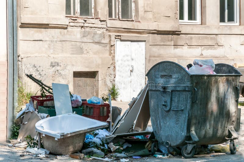 Pilha grande do lixo e da sucata despejados na rua perto da lata do contentor