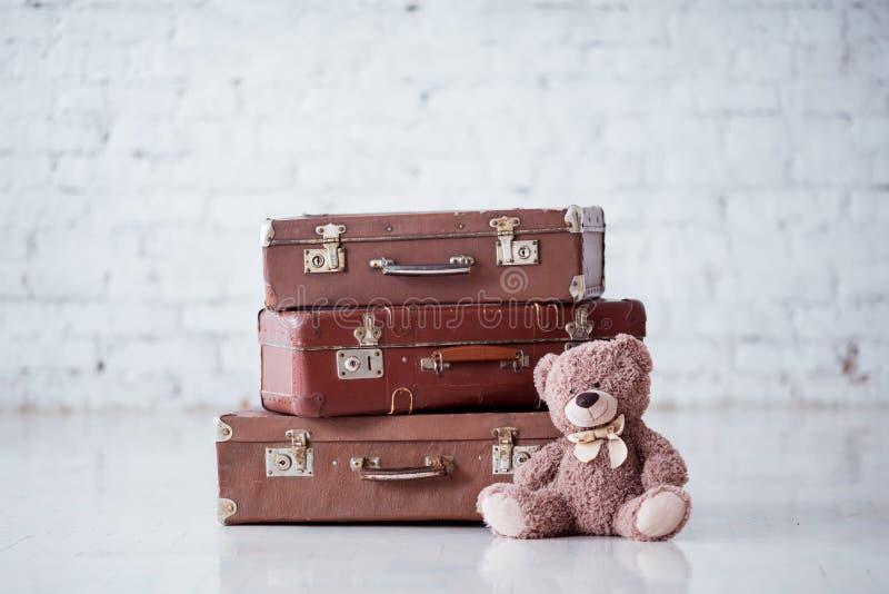 Teddy bear near stack of three brown retro suitcases on white floor. Teddy bear near stack of three brown retro suitcases on white floor.