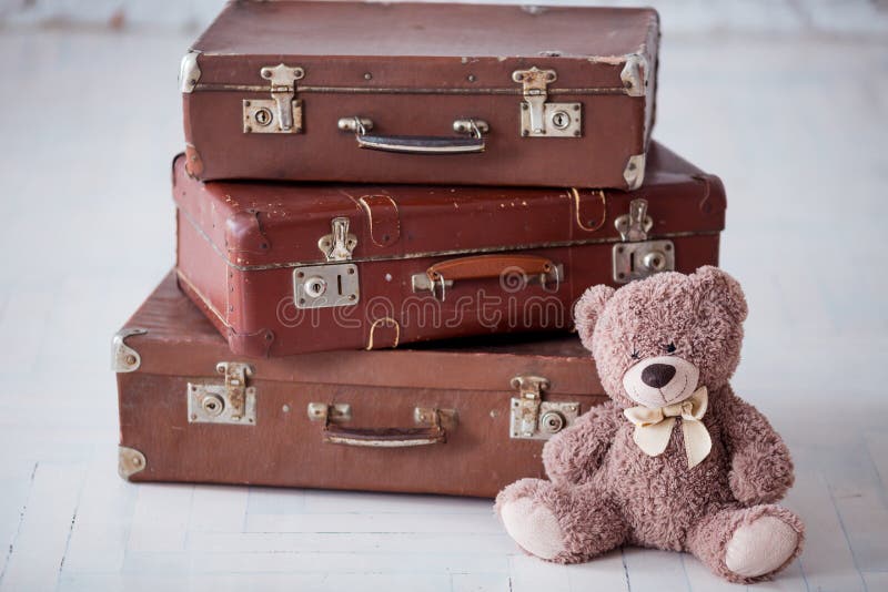 Teddy bear near stack of three brown retro suitcases on white floor. Teddy bear near stack of three brown retro suitcases on white floor.