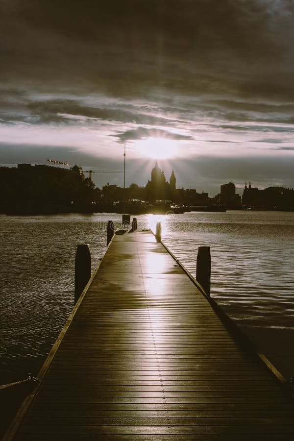 Pilier en bois avec des bateaux au coucher du soleil dans le dock d'Amsterdam Silhouettes de ville d'Amsterdam en égalisant la lu images stock Pilier en bois avec des bateaux au coucher du soleil dans le dock d'Amsterdam Silhouettes de ville d'Amsterdam en égalisant la lu images stock