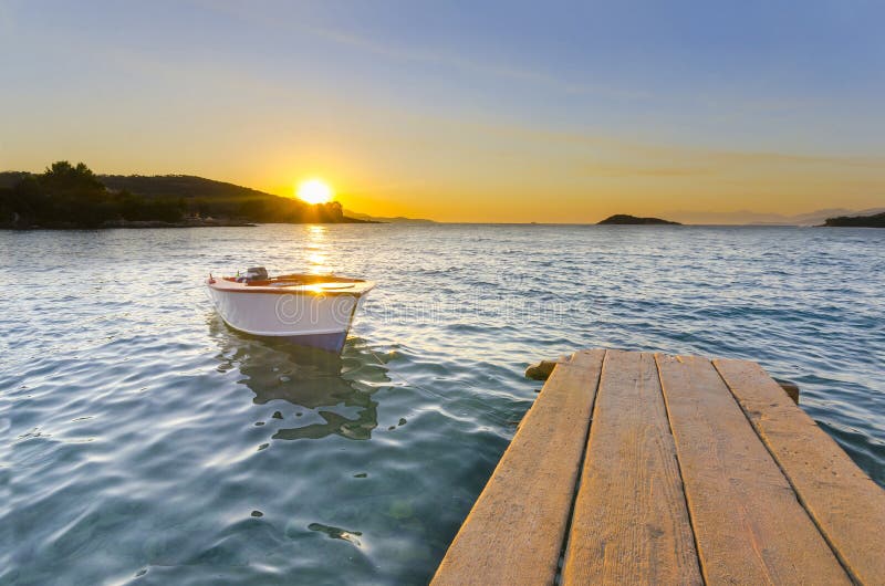 Pilier ou jetée en bois et un bateau sur un coucher du soleil de lac image stock Pilier ou jetée en bois et un bateau sur un coucher du soleil de lac image stock
