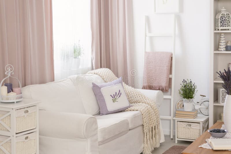 Pillows and blanket on white sofa in pink living room interior with drapes and flowers. Real photo concept