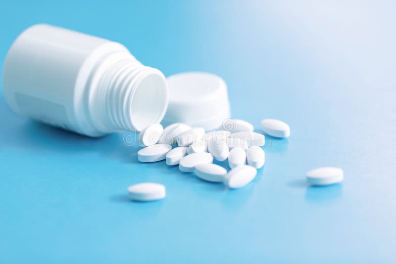 Pills spilled out of white bottle on light blue background with copy space. Medical healthcare concept