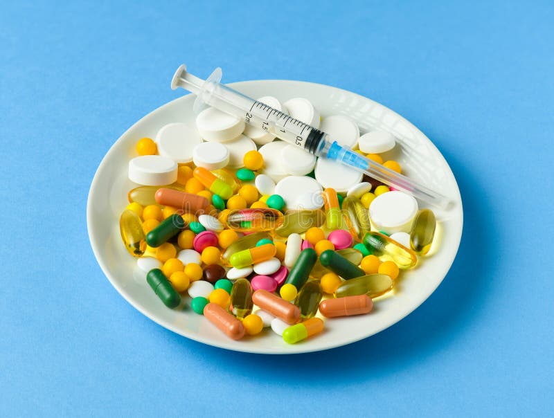 Pills, tablets, syringe, vitamins, drugs, medicine in a white dish for medical treatment. Blue background