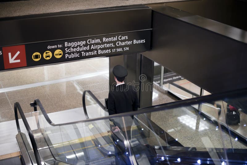 Pilot goes down with suitcase on airport escalator stock photo